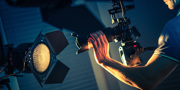 Videographer holding a camera rig next to a film studio light source.